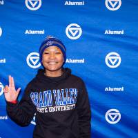 GVSU Alumni standing in front of backdrop smiling giving Anchor Up sign to camera